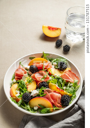 Fresh salad with peaches, arugula, feta, prosciutto and berries in a plate on a light background 131787515