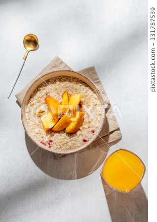 Oatmeal with peaches and nuts  in a bowl on a light background with honey 131787539