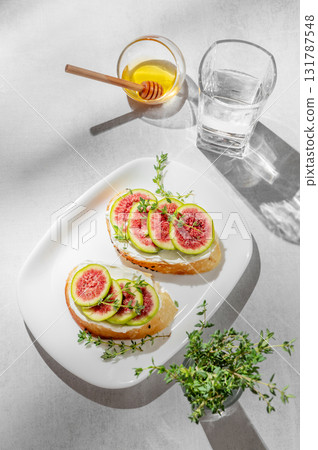 Sweet toasts with fresh figs, cream cheese, thyme, and honey on a light background. Sweet toasts with fresh figs, cream cheese, thyme, and honey on a light background. 131787548