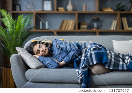 Young Muslim woman resting and sleeping at home on the sofa covered with a blanket. Young Muslim woman resting and sleeping at home on the sofa covered with a blanket. 131787957