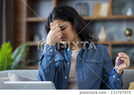A woman with her hand on her nose, holding her glasses in her other hand, feeling eye strain. 131787978