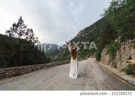 A woman in a white dress is standing on a road, waving her hand 131788572