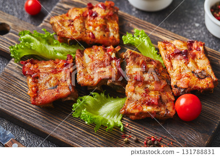 Grilled baked pork ribs with spices and vegetables on wooden cutting board on dark background. American food concept. 131788831