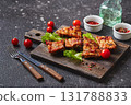 Grilled baked pork ribs with spices and vegetables on wooden cutting board on dark background. American food concept. 131788833