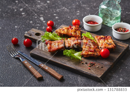 Grilled baked pork ribs with spices and vegetables on wooden cutting board on dark background. American food concept. 131788833