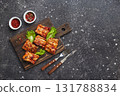 Grilled baked pork ribs with spices and vegetables on wooden cutting board on dark background. American food concept. Top view, copy space. 131788834