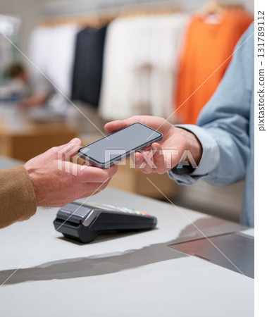 Focused customer making seamless mobile phone payment in retail store. man hand holds smartphone over contactless reader for fast and convenient purchase 131789112