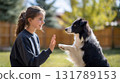 Happy teenager teaching Border Collie dog new trick. Young girl giving high five to clever canine friend outdoors in sunny backyard, showing friendship and trust 131789153