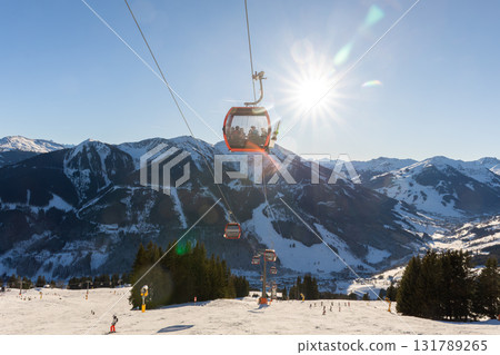 Sunny winter day on alpine slope with skis and snowboards resting near gondola station. Bright sunlight, blue sky, and mountain panorama create atmosphere of adventure, freedom, and relaxation 131789265