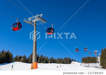 Sunny winter day on alpine slope with skis and snowboards resting near gondola station. Bright sunlight, blue sky, and mountain panorama create atmosphere of adventure, freedom, and relaxation 131789267