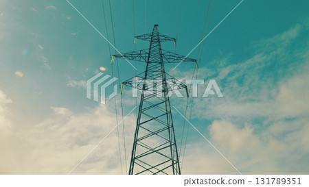 A tall electricity pylon stands against a bright blue sky, highlighting its significance A tall electricity pylon stands against a bright blue sky, highlighting its significance 131789351