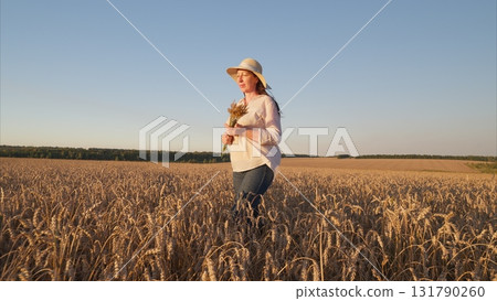 A woman walking gracefully in a wheat field surrounded by vibrant sunflowers during sunset 131790260