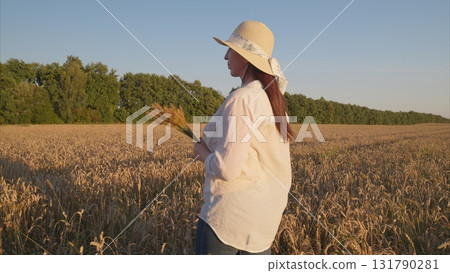 A captivating image of a woman walking gracefully in a wheat field during a stunning sunset 131790281