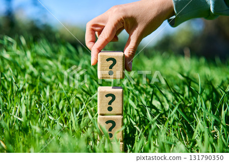 Hand placing wooden cube with question mark symbol on pyramid stack Hand placing wooden cube with question mark symbol on pyramid stack 131790350