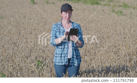 A Woman Utilizing a Tablet While Standing in a Vast Field Full of Growing Crops Nearby A Woman Utilizing a Tablet While Standing in a Vast Field Full of Growing Crops Nearby 131791798