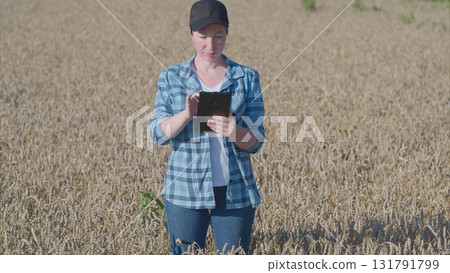 A person is utilizing a tablet device in a broad field filled with various healthy crops 131791799