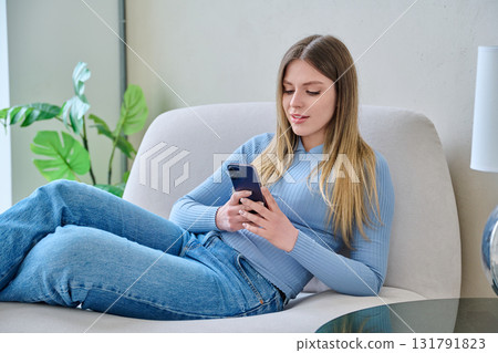 Young woman sitting at home in chair using smartphone Young woman sitting at home in chair using smartphone 131791823