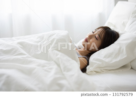 一位女士睡在白色的床上，周圍環繞著晨光 131792579