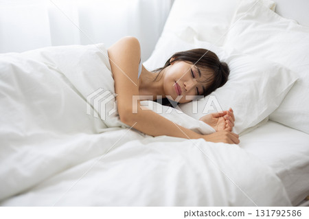 一位女士睡在白色的床上，周圍環繞著晨光 131792586
