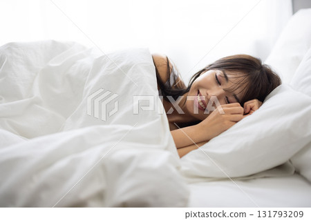 A woman sleeping in a white bed surrounded by morning light 131793209