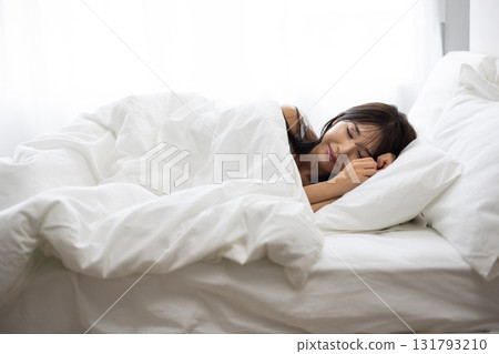 A woman sleeping in a white bed surrounded by morning light 131793210
