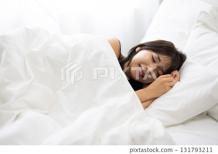A woman sleeping in a white bed surrounded by morning light 131793211