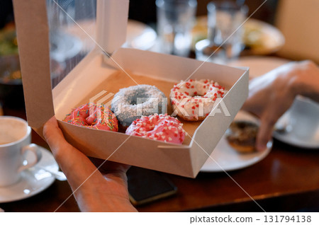 A hand holds a box with four colorful glazed donuts A hand holds a box with four colorful glazed donuts 131794138