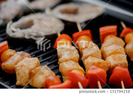Fish skewers with tomatoes and steaks on a black barbecue grill Fish skewers with tomatoes and steaks on a black barbecue grill 131794158