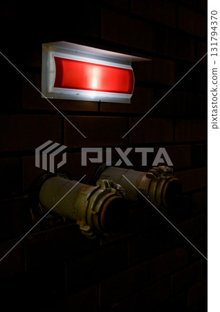 Dark interior with emergency lighting and utility pipes. 131794370