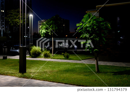 Nighttime landscaping of a residential complex courtyard with lawn, trees 131794379