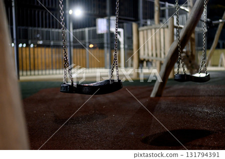 Children's playground with wooden swings and a slide at night. 131794391