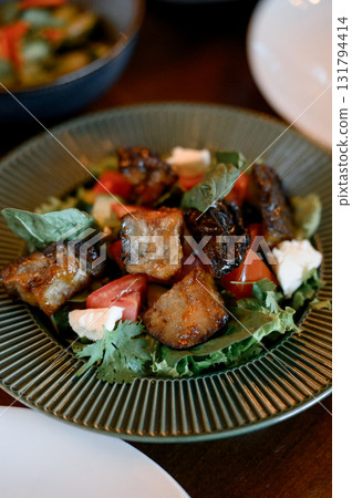 Fresh salad with pieces of meat, tomatoes and feta cheese in a dark plate. 131794414