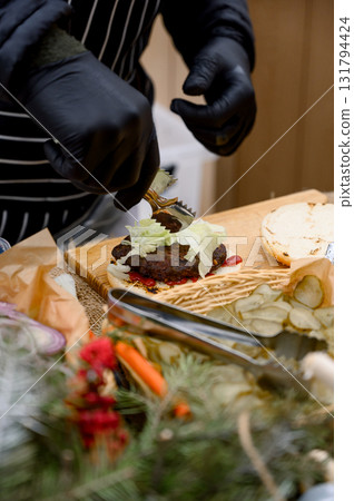 A chef in black gloves and an apron prepares a classic burger. A chef in black gloves and an apron prepares a classic burger. 131794424