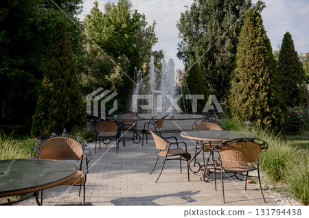 A summer cafe with wicker chairs and wrought iron tables near a fountain 131794438