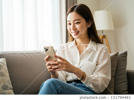 Woman sitting on a sofa and looking at a smartphone Woman sitting on a sofa and looking at a smartphone 131794461