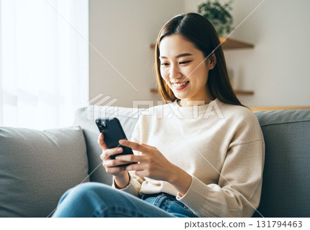 Woman sitting on a sofa and looking at a smartphone 131794463
