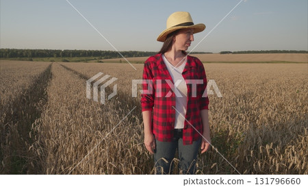 A woman stands in a beautiful wheat field, elegantly wearing a straw hat, enjoying the scenery A woman stands in a beautiful wheat field, elegantly wearing a straw hat, enjoying the scenery 131796660