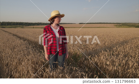 A Woman Standing in a Wheat Field, Elegantly Wearing a Straw Hat Under the Bright Sun 131796663
