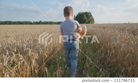 A child joyfully exploring a vast golden wheat field while holding a toy in hand 131796713