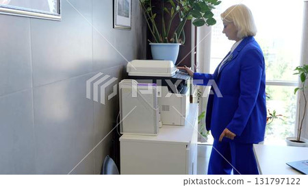 Efficient and productive, a businesswoman in a blue suit utilizing a multifunction printer in a bright, contemporary office setting 131797122