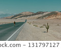A lone hiker walks down a desert road towards distant mountains 131797127