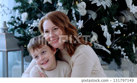 Mother and son share a joyful moment in front of their beautifully decorated christmas tree, embracing the holiday magic. A day with family before Christmas. New Year's Eve with family 131797149