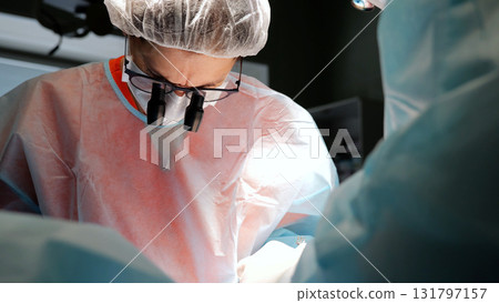 Skilled surgeon wearing surgical loupes is performing a precise surgical procedure in a sterile operating room 131797157