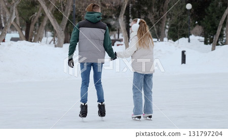 Young couple enjoys a romantic day out, holding hands while ice skating in a snowy winter park, creating a heartwarming scene of togetherness and leisure Young couple enjoys a romantic day out, holding hands while ice skating in a snowy winter park, creating a heartwarming scene of togetherness and leisure 131797204