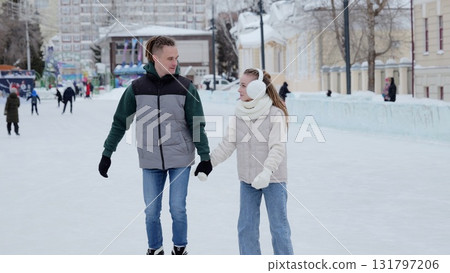 Cheerful couple gliding hand in hand across frosty outdoor skating rink, sharing joyful winter moment in urban landscape Cheerful couple gliding hand in hand across frosty outdoor skating rink, sharing joyful winter moment in urban landscape 131797206