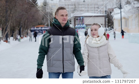 Cheerful couple walking hand in hand on snow covered ice rink, sharing warm embrace amid winter holiday celebration and festive surroundings 131797207