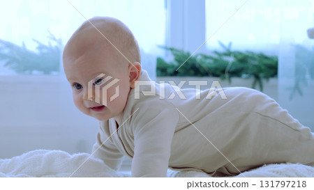 Curious and playful baby boy crawling near a christmas tree in a warm, festive room filled with light. Baby crawling on the floor in a bright room Curious and playful baby boy crawling near a christmas tree in a warm, festive room filled with light. Baby crawling on the floor in a bright room 131797218