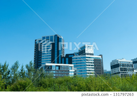 Modern Architectural Designs of High-Rise Buildings Surrounded by Lush Greenery Against a Clear Blue Sky Modern Architectural Designs of High-Rise Buildings Surrounded by Lush Greenery Against a Clear Blue Sky 131797263