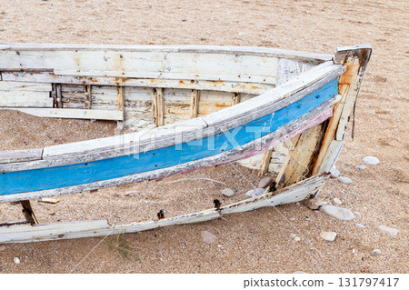 An old, weather-beaten boat rests on a sandy shore, its blue stripe peeling away. 131797417