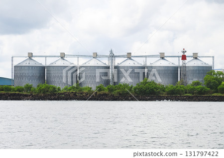 Row of large metal grain silos sits on a rocky shore, Row of large metal grain silos sits on a rocky shore, 131797422